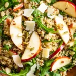 A wooden bowl filled with Apple Salad textures in a Honey Mustard Quinoa Apple Salad with Crispy Shallots, tossed with honey mustard dressing and crunchy seeds.