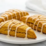 A white plate holds golden Pumpkin Cinnamon Scones drizzled with Maple Glaze beside a mug, showing tender Scones that fit any Pumpkin Scones Recipe for cozy Fall Baking and classic Autumn Flavors.