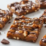 Salted Caramel Pretzel Bark squares with chocolate drizzle and flaky sea salt on a marble surface, sweet and salty homemade candy