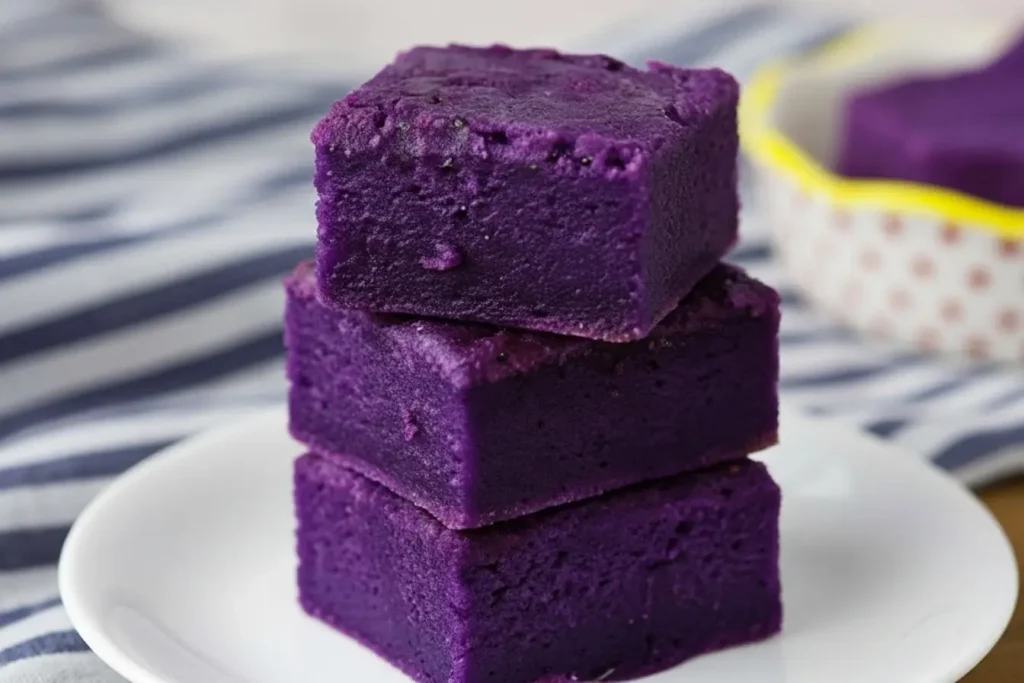Ube Mochi Recipe, three vibrant purple mochi bars stacked on a white plate, chewy Butter Mochi texture, Filipino Food Dessert idea for easy baked ube squares