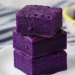 Ube Mochi Recipe - How to Bake Chewy Purple Yam Mochi Bars at Home 5 Ube Mochi Recipe, three vibrant purple mochi bars stacked on a white plate, chewy Butter Mochi texture, Filipino Food Dessert idea for easy baked ube squares