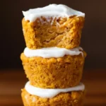 Healthy Flourless Pumpkin Muffins 5 Stack of three healthy flourless Pumpkin Muffins with creamy frosting, top muffin bitten to show moist crumb, gluten free fall breakfast treat.