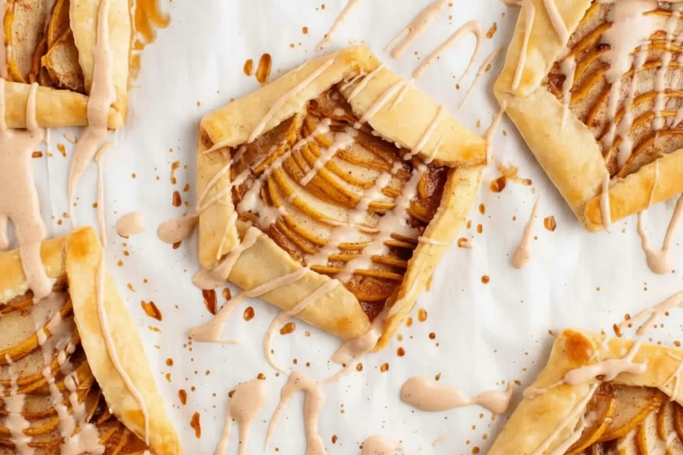 Easy Pear Galettes on parchment, rustic puff pastry squares filled with thinly sliced pears and cinnamon, finished with a light glaze drizzle, perfect quick pear dessert