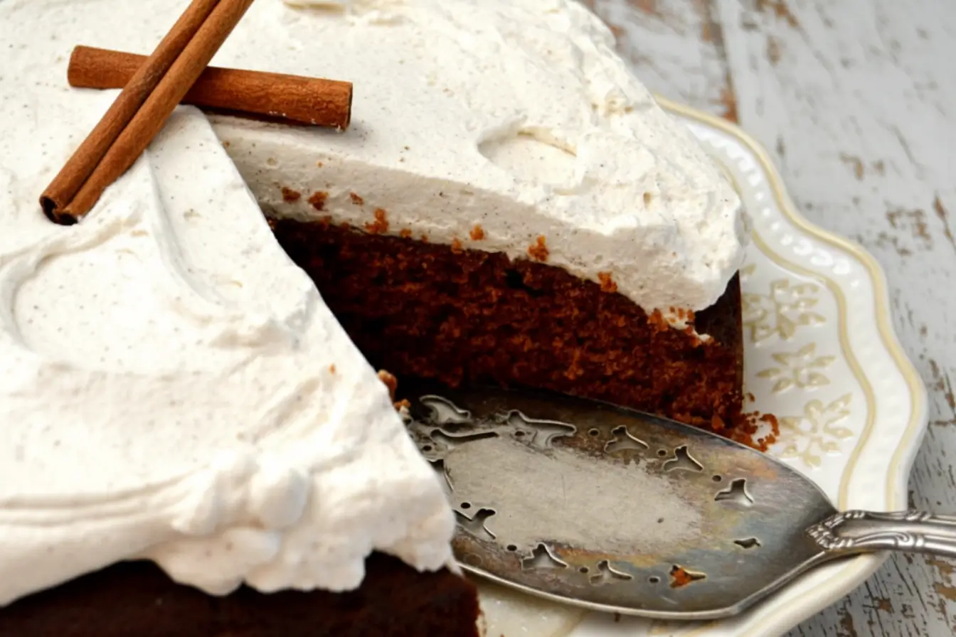 Gingerbread Molasses Cake topped with creamy cinnamon molasses frosting on a patterned plate, served with coffee and cinnamon sticks