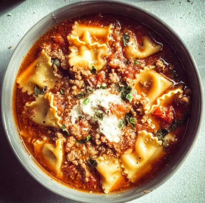 Delicious Crockpot Lasagna Soup in a bowl with fresh herbs and cheese on top.